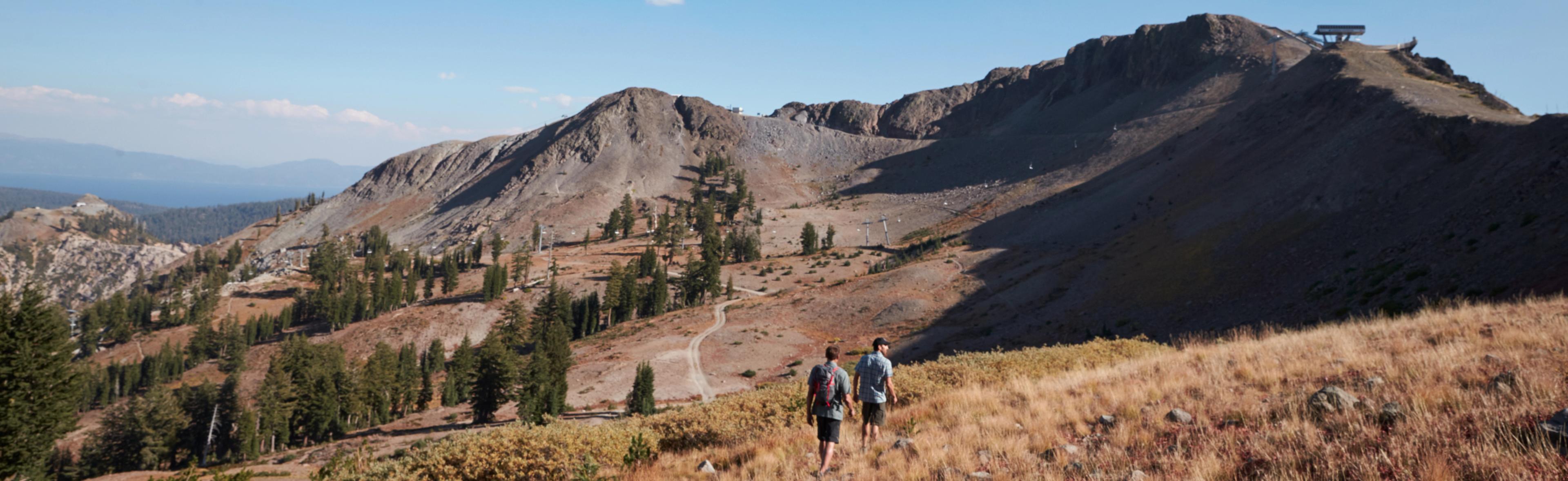 Two men hiking down a dirt path dressed in KUHL men's summer hiking clothing