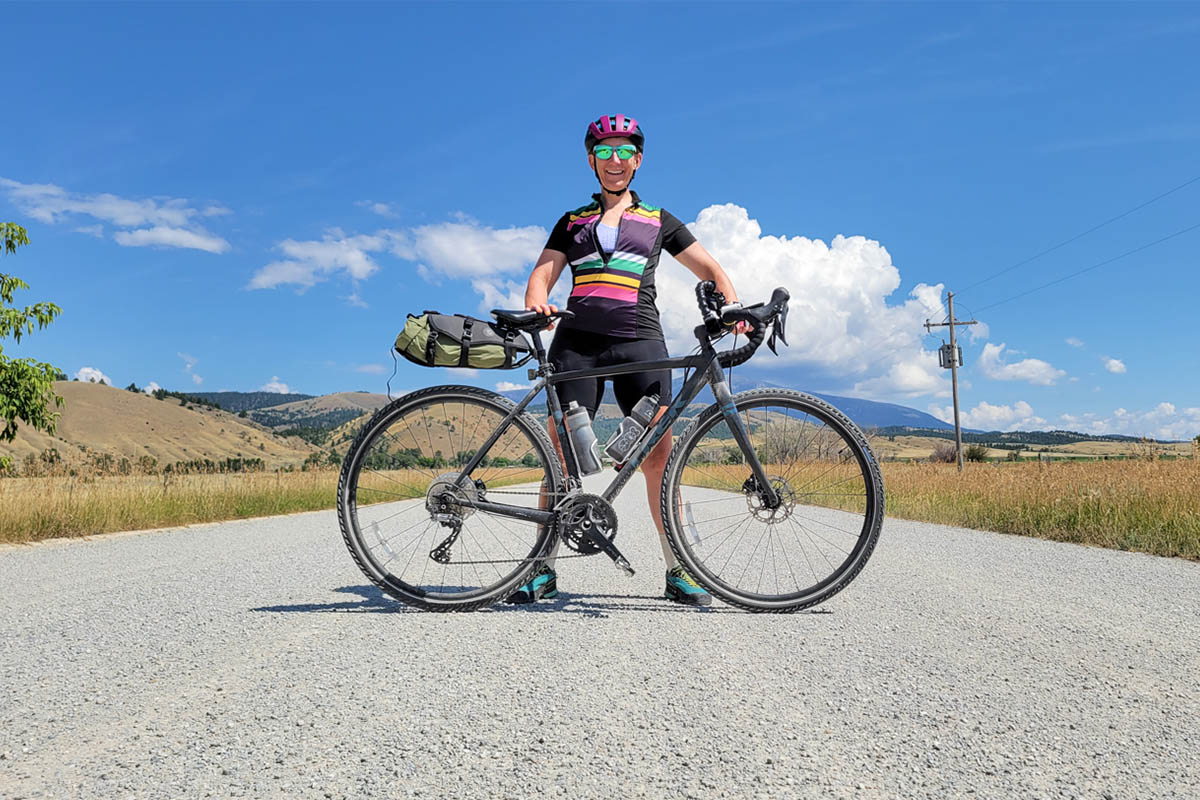 A cyclist standing in the middle of a road on a sunny day