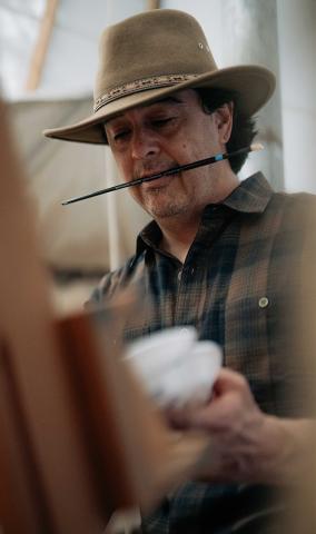 Manny placing a brush on a palette while holding another brush between his teeth