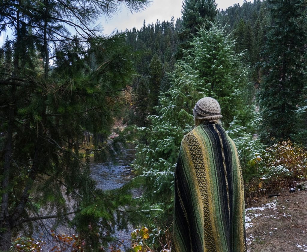 A woman covered in a blanket standing in the woods.