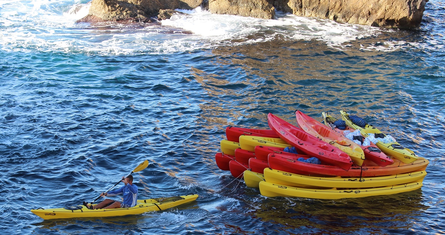 man in yellow kayak pulling red and yellow kayaks