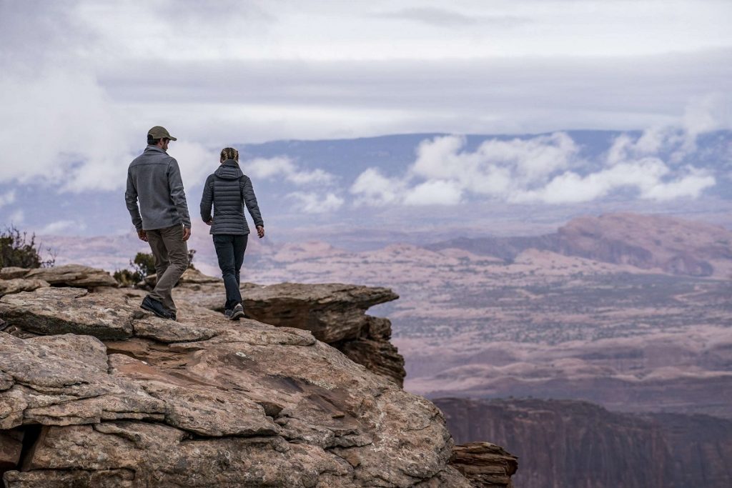 man and woman walking on high cliff in front of blue sky