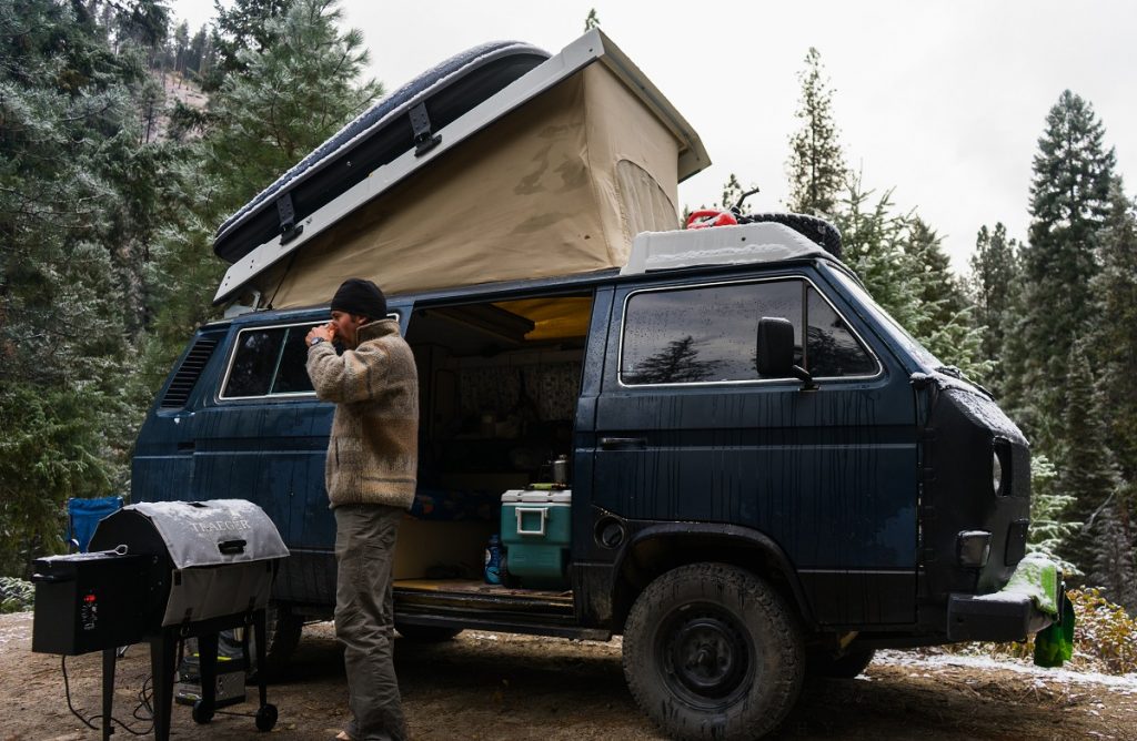 a man in KÜHL pants standing in fron of blue camper van