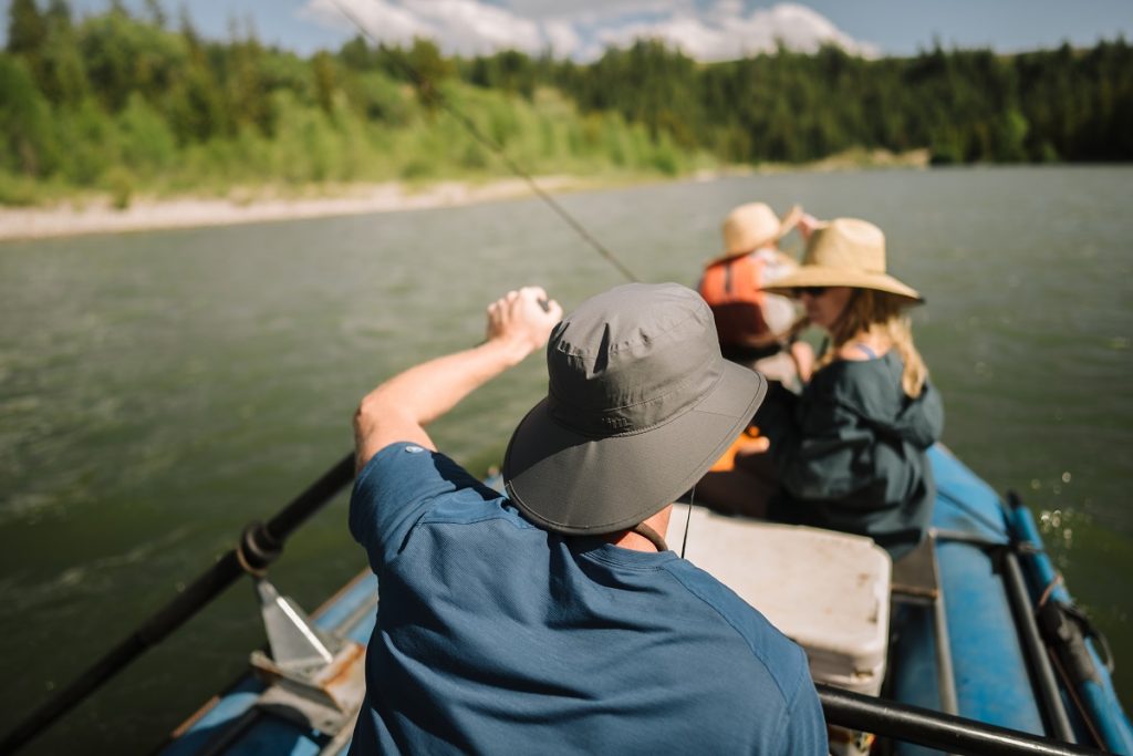 man wearing KÜHL sun hat holding paddle on raft