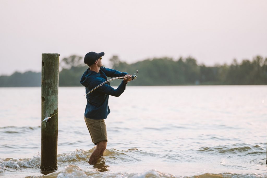 man in KÜHL clothing casting fishing lure into lake