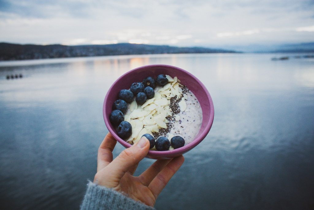 woman holding pink ceramic bowl in front of body of water