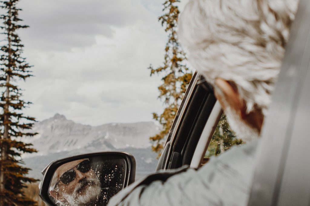 man with gray hair and beard reflecting in car mirror