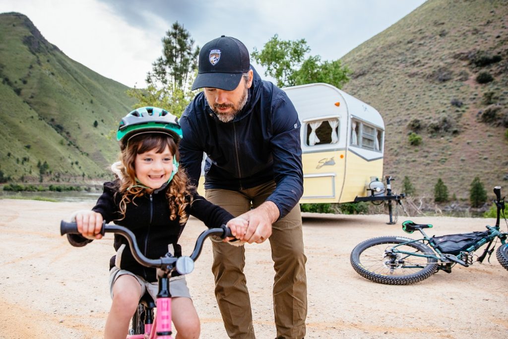 man in KÜHL clothing holding daughter on bicycle