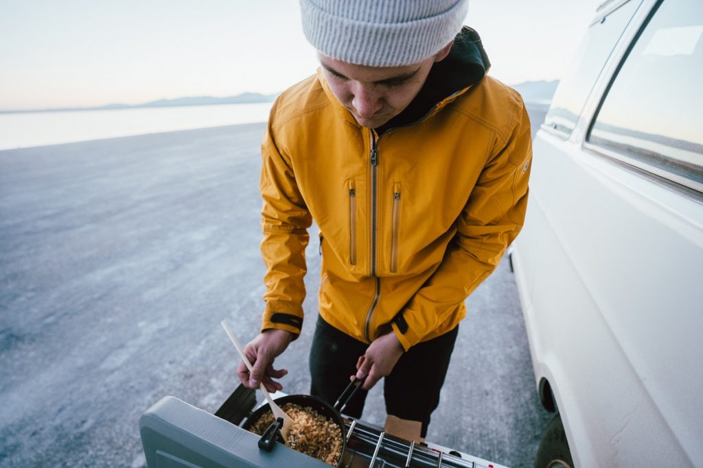 man in yellow KÜHL jacket preparing oatmeal outdoors