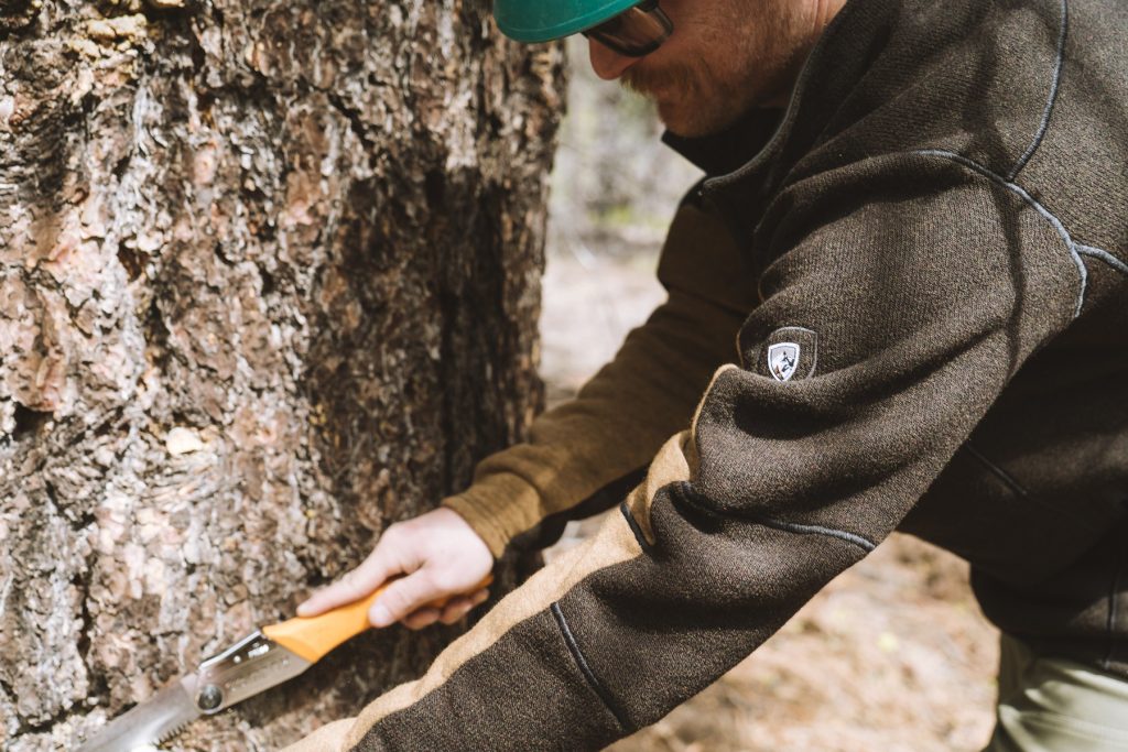 Glenn cutting a branch while building a mountain biking trail in KUHL men's clothing