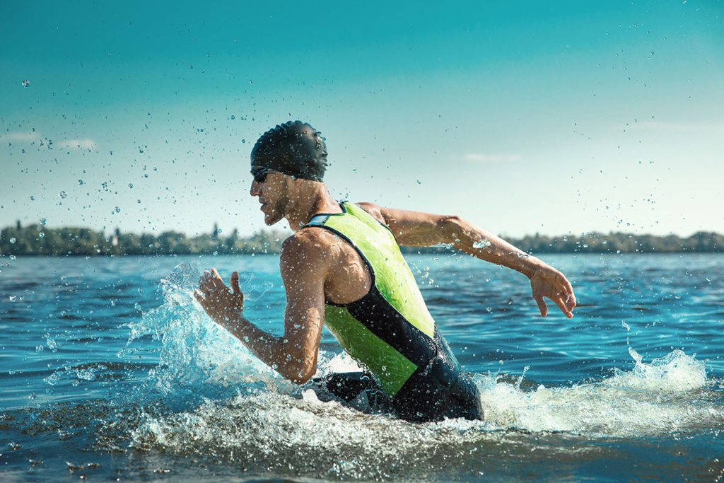 Man wearing swim equipment practicing triathlon on the beach in summer's day