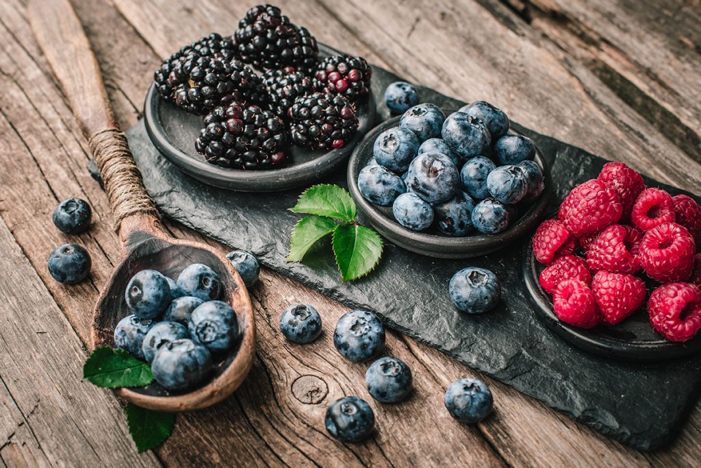 Fresh berries with raspberries, blueberries, blackberries in bowl on a stone stand on wood background.